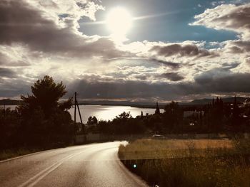 Road by trees against sky during sunset