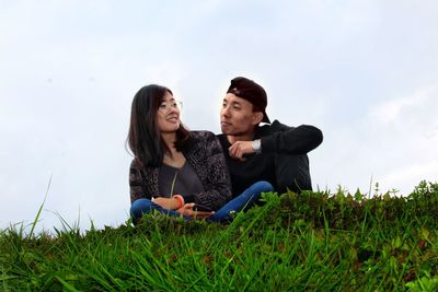 Low angle view of man sitting with woman on grassy field against sky