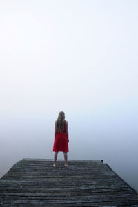 Rear view of woman standing on pier by lake in foggy weather