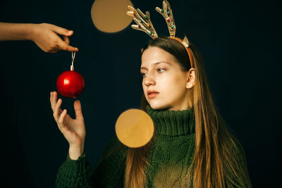 A teenage girl in reindeer horns looks at the hand with a red christmas ball