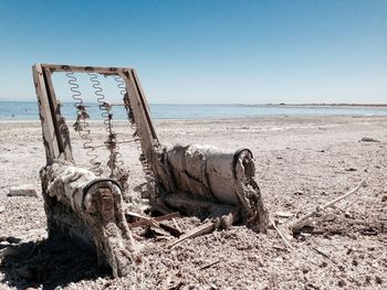 Abandoned weathered armchair at beach against sky