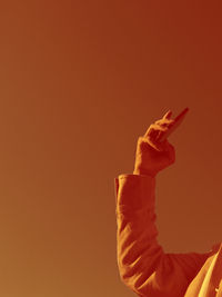 Close-up of hand holding orange against sky