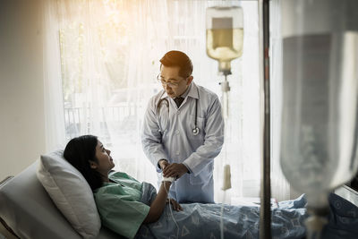 Doctor consoling patient lying on bed at hospital