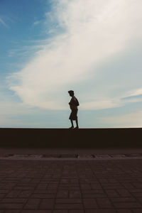 Man walking on wall by sidewalk against sky