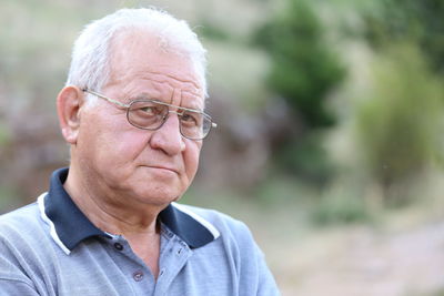 Portrait of serious senior man wearing eyeglasses standing at park