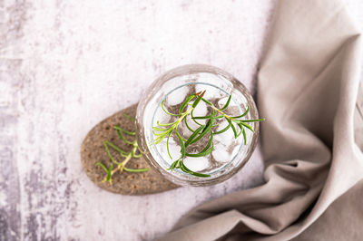 Close up of gin tonic with ice and rosemary in a glass on a stone on the table top view