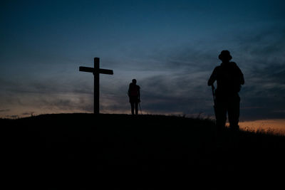 Silhouette men standing on cross against sky during sunset