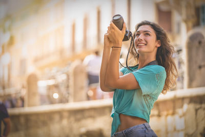 Young woman photographing while using phone in city