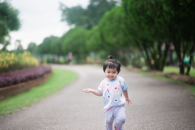 Cute smiling girl walking on road against trees