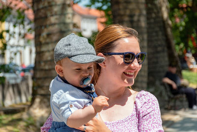 Portrait of mother holding her baby boy in park in city