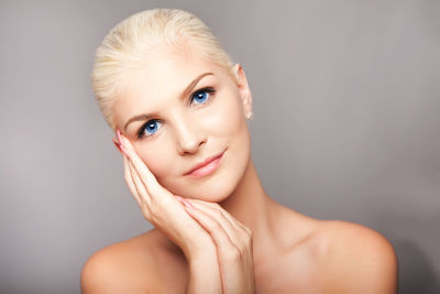 Portrait of young beautiful woman with glowing skin against gray background