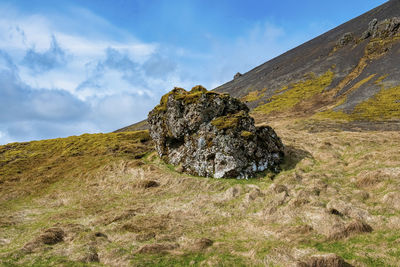 Close-up of rock formation on grassy landscape of mountain against blue sky