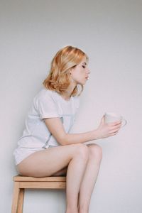 Young woman looking down while sitting against white background