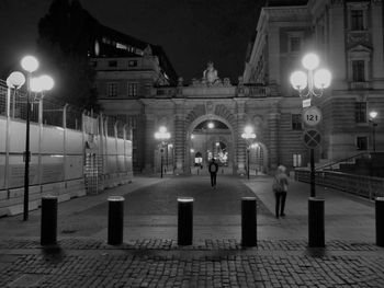 People walking on illuminated street amidst buildings at night