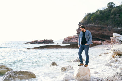 Full length of man standing on rock at beach against sky