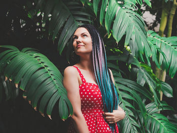 Thoughtful woman with dreadlocks standing against plants