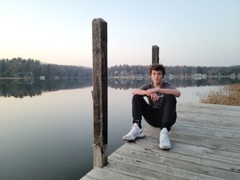 Full length of young man sitting on wood against lake