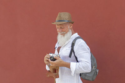 Smiling man holding camera while standing against wall