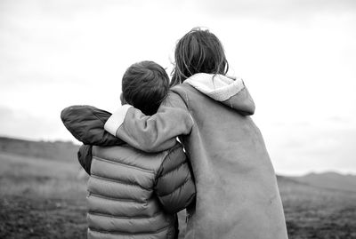 Rear view of siblings in warm clothing standing on field against sky