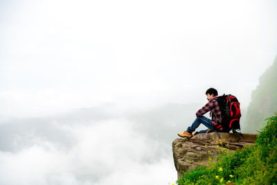 Men sitting on rock against sky