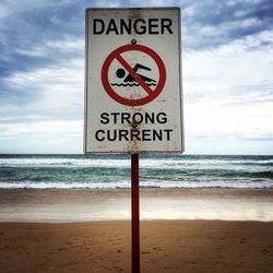 Low angle view of warning sign at beach against sky