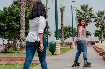 Smiling woman with friends skateboarding on footpath in park