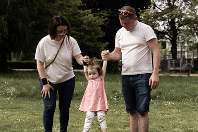 Portrait of one caucasian parents raising their little daughter while standing in a park 