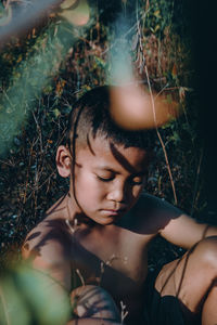 Shirtless boy sitting against plants