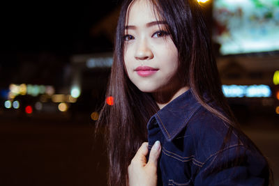 Portrait of beautiful young woman standing on street at night