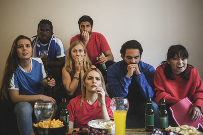 Worried male and female friends watching sport while sitting on sofa at home