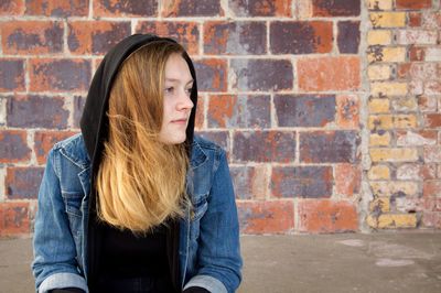 Young woman looking away against brick wall