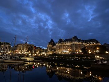 Illuminated buildings by river against sky at night