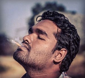 Close-up of young man with closed eyes smoking cigarette