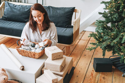 Young adult forty years woman with present gift box in living room with christmas tree at home