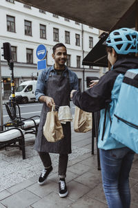 Delivery woman collecting order from male owner while standing on sidewalk