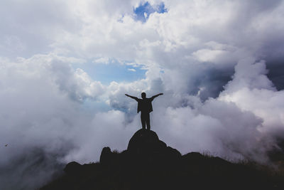 Low angle view of silhouette man standing on rock against sky