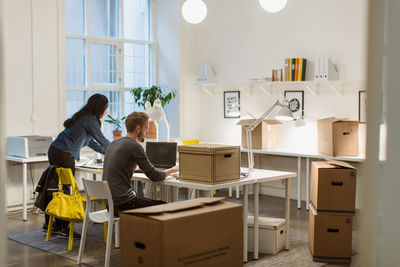 Business colleagues working at desk amidst cardboard boxes in illuminated creative office