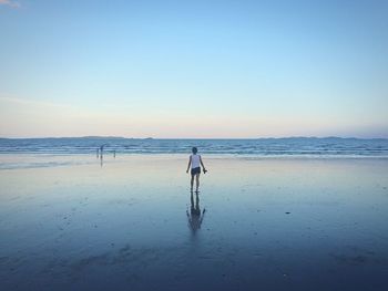 Rear view of woman walking on beach against sky