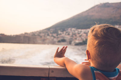 Rear view portrait of boy in water against sky