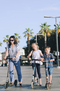 Happy family lifestyle. mother, boy, girl in city. ride scooters. laughing on a summer. fun