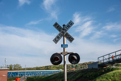Railroad crossing sign on field against blue sky