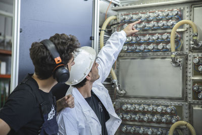 Young technician pointing at stainless steel bottles and discussing with colleague in industry