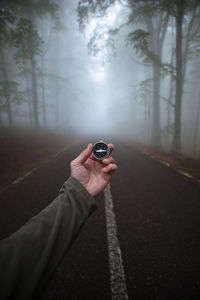 A first-person view of a man's hand holds a compass against the background of foggy forest
