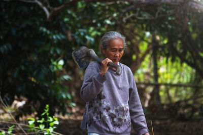 Mature woman with shovel standing in forest