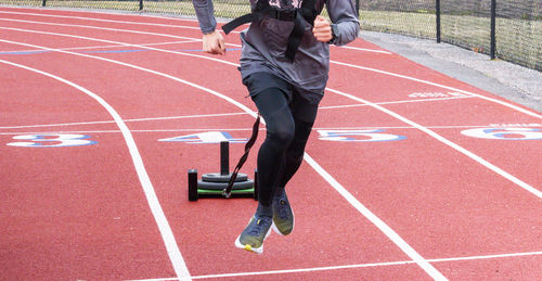 Front view of a high school boy running while pulling a sled with weights on a track during practice