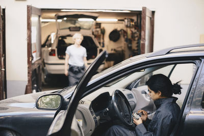 Side view of female mechanic using mobile phone while sitting in car