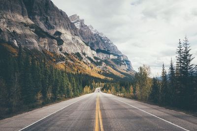 Empty road along rocky mountains against sky