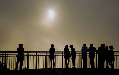 Silhouette people standing by railing against clear sky