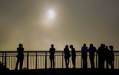 Silhouette people standing by railing against clear sky