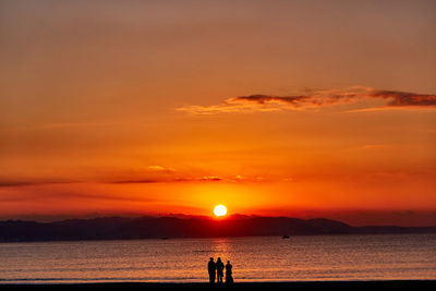 Silhouette people on beach against orange sky